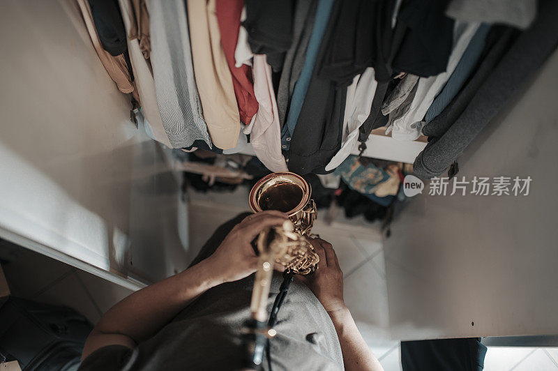 top view of asian chinese mid adult man practicing saxophone facing his wardrobe as soundproof to reduce the sounds disturbing his neighbor  in his apartment